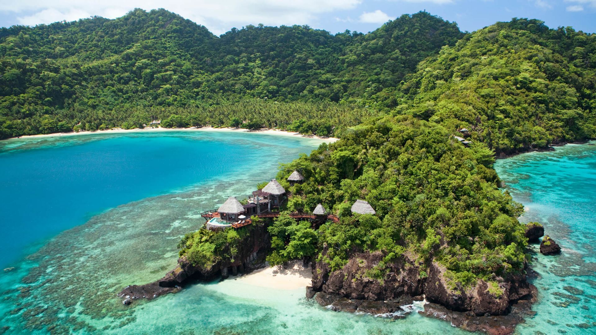 Tropical island with lush green vegetation, blue ocean, and buildings on a rocky outcropping. Fiji