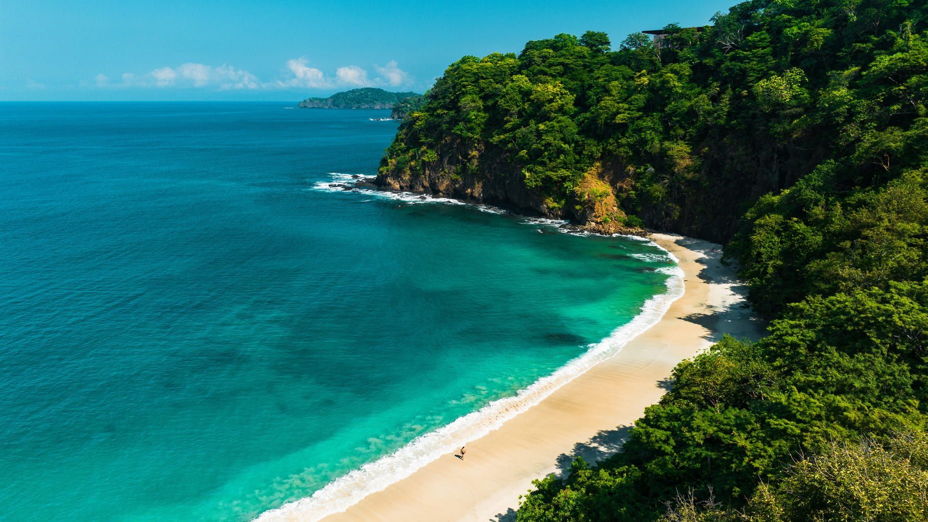 Tropical beach with turquoise water, white sand, and lush green cliffs under a clear sky. Four Seasons Resort Costa Rica 