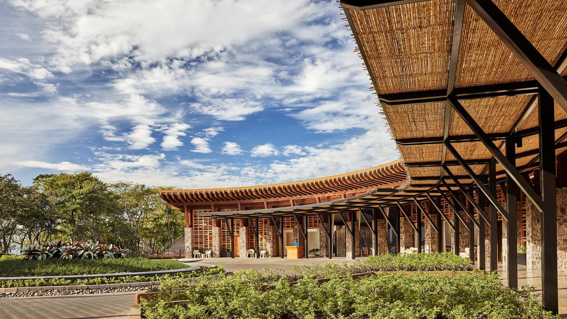 Modern building with red-tiled roof beside a landscaped courtyard under a partly cloudy sky. Four Seasons Resort Costa Rica 