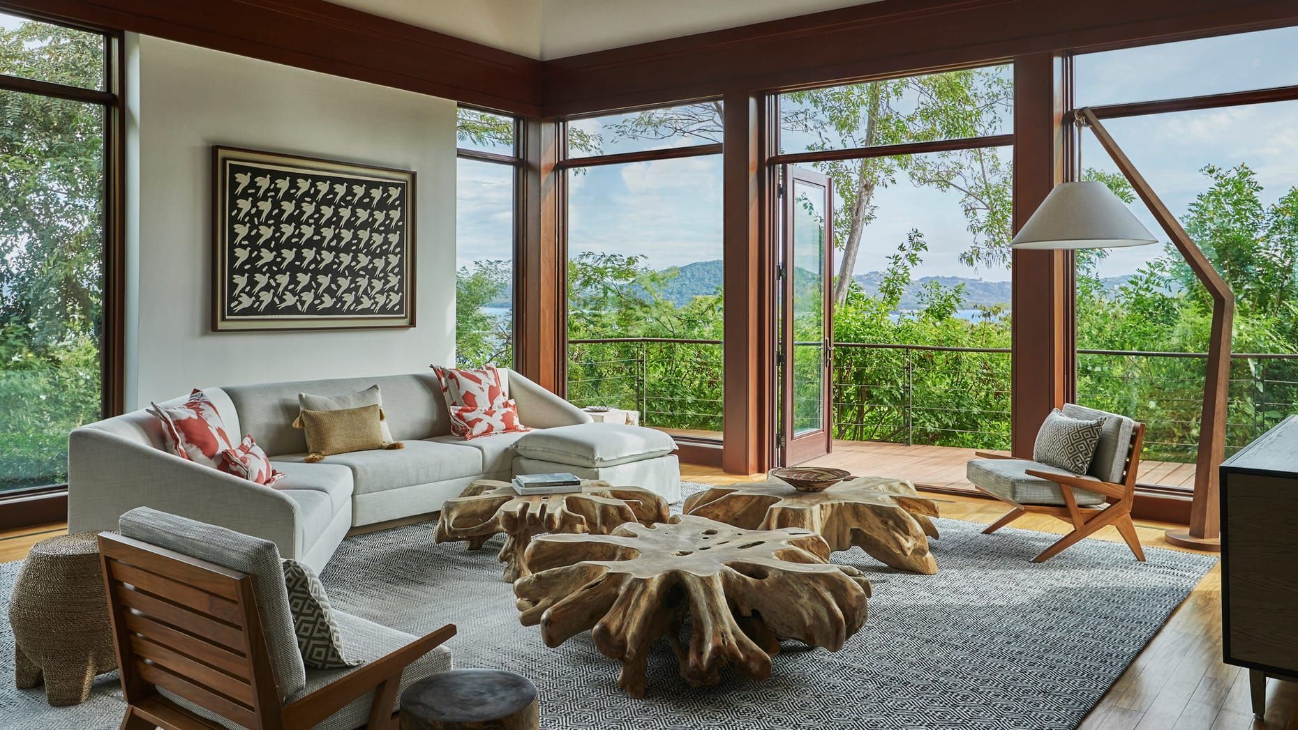 Bright living room with large windows, white sofa, wood stump coffee table, and lush green forest view. Four Seasons Resort Costa Rica 