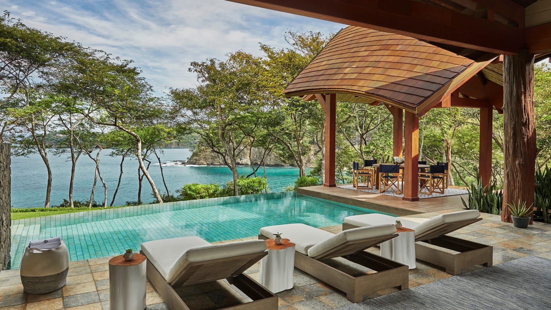 Infinity pool overlooking turquoise sea, with shaded lounge chairs and a wooden gazebo on the deck. Four Seasons Resort Costa Rica 
