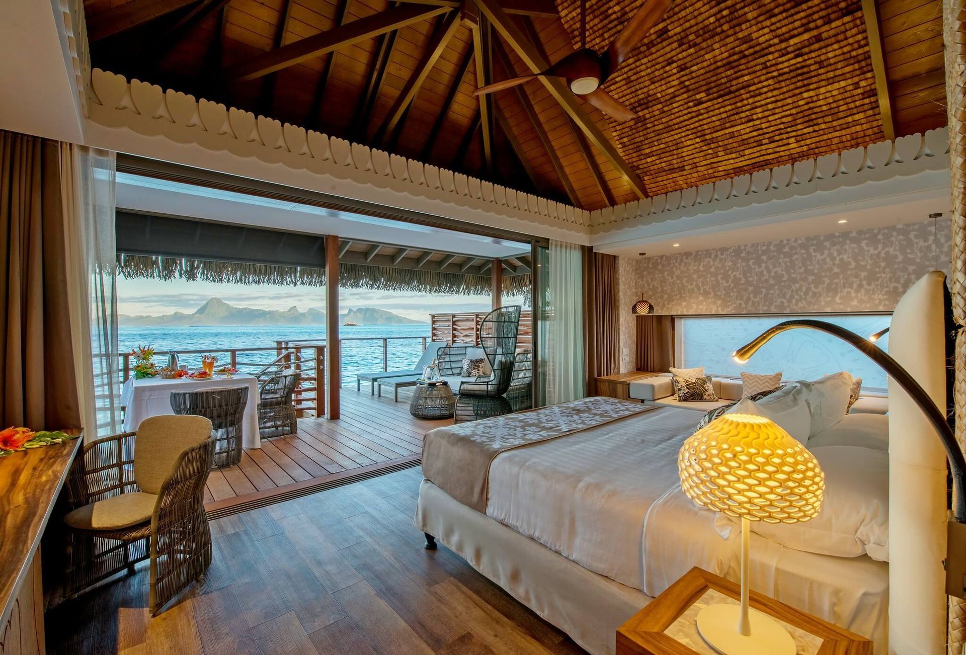 A luxurious bedroom in an overwater bungalow with a large bed, wicker furniture, and an open terrace overlooking the sea. Room InterContinental, Tahiti