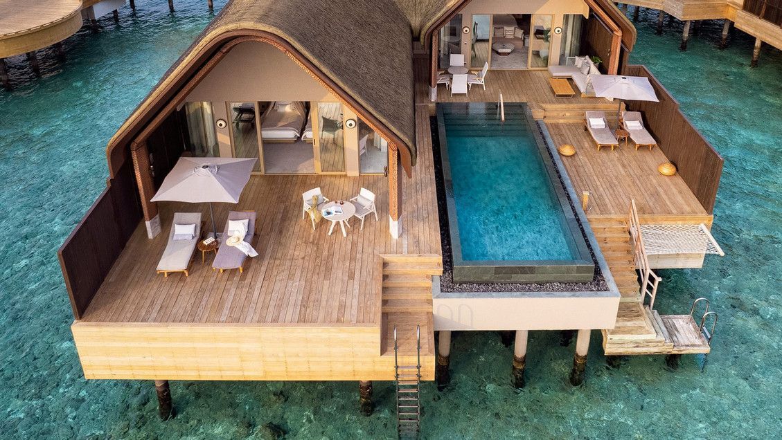 Overwater bungalow with a pool, deck, and chairs in turquoise water. JOALI Being