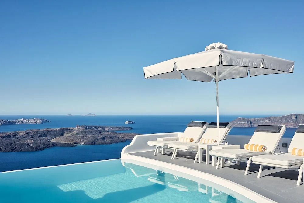 Infinity pool with lounge chairs and umbrella overlooking the Aegean Sea in Santorini. Katikies Santorini
