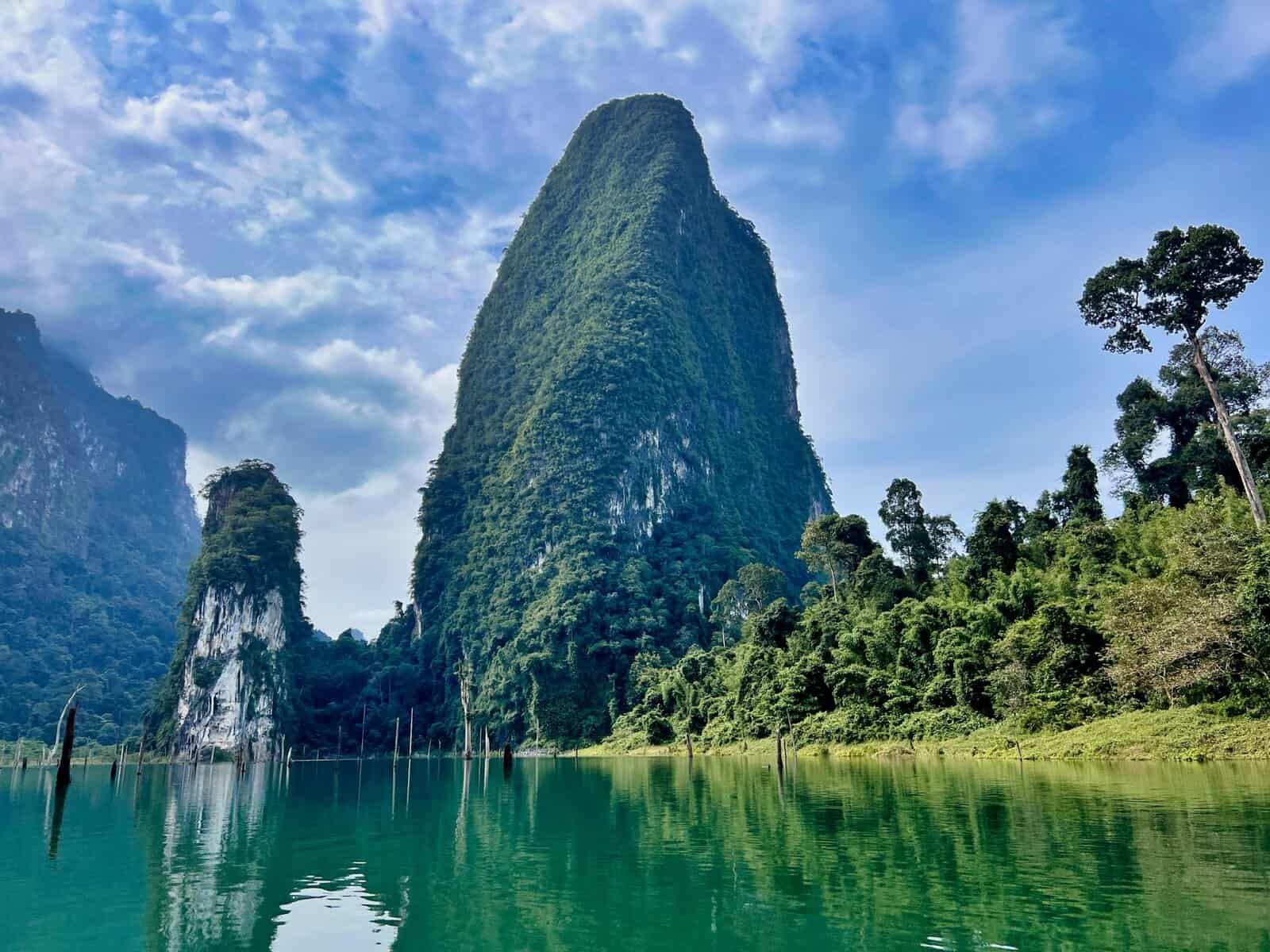 Emerald lake with lush green mountains under a cloudy sky.