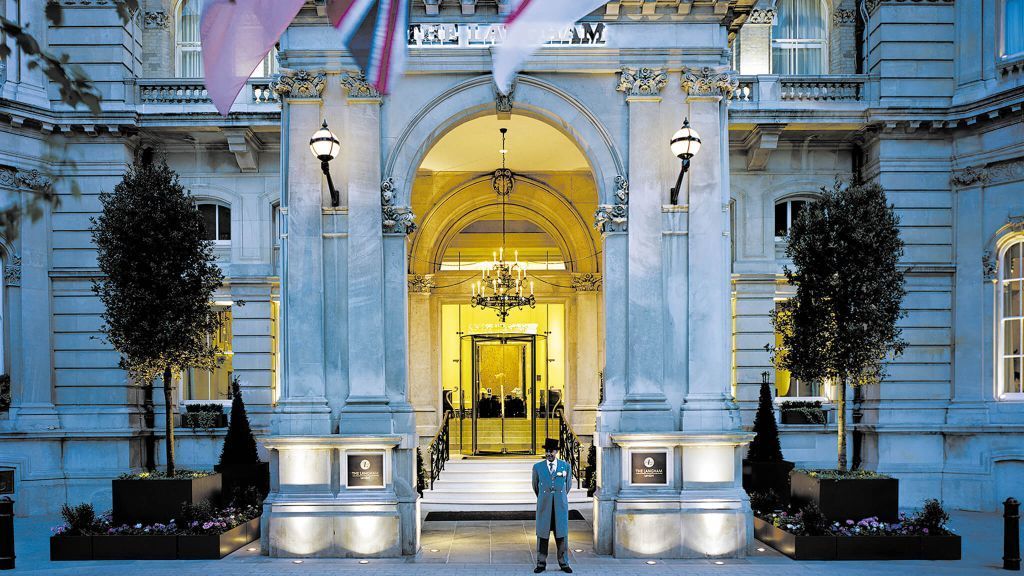 Elegant hotel entrance with archway, flags, and doorman standing. Langham Hotel