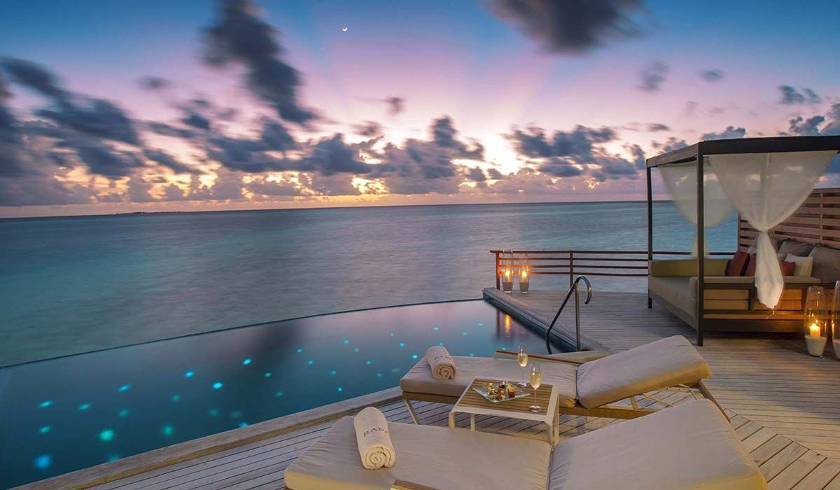 Infinity pool overlooking ocean at sunset with lounge area. Maldives