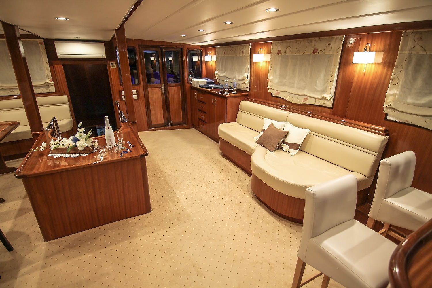 Interior of a yacht with a beige sofa, wooden paneling, and bar stools.