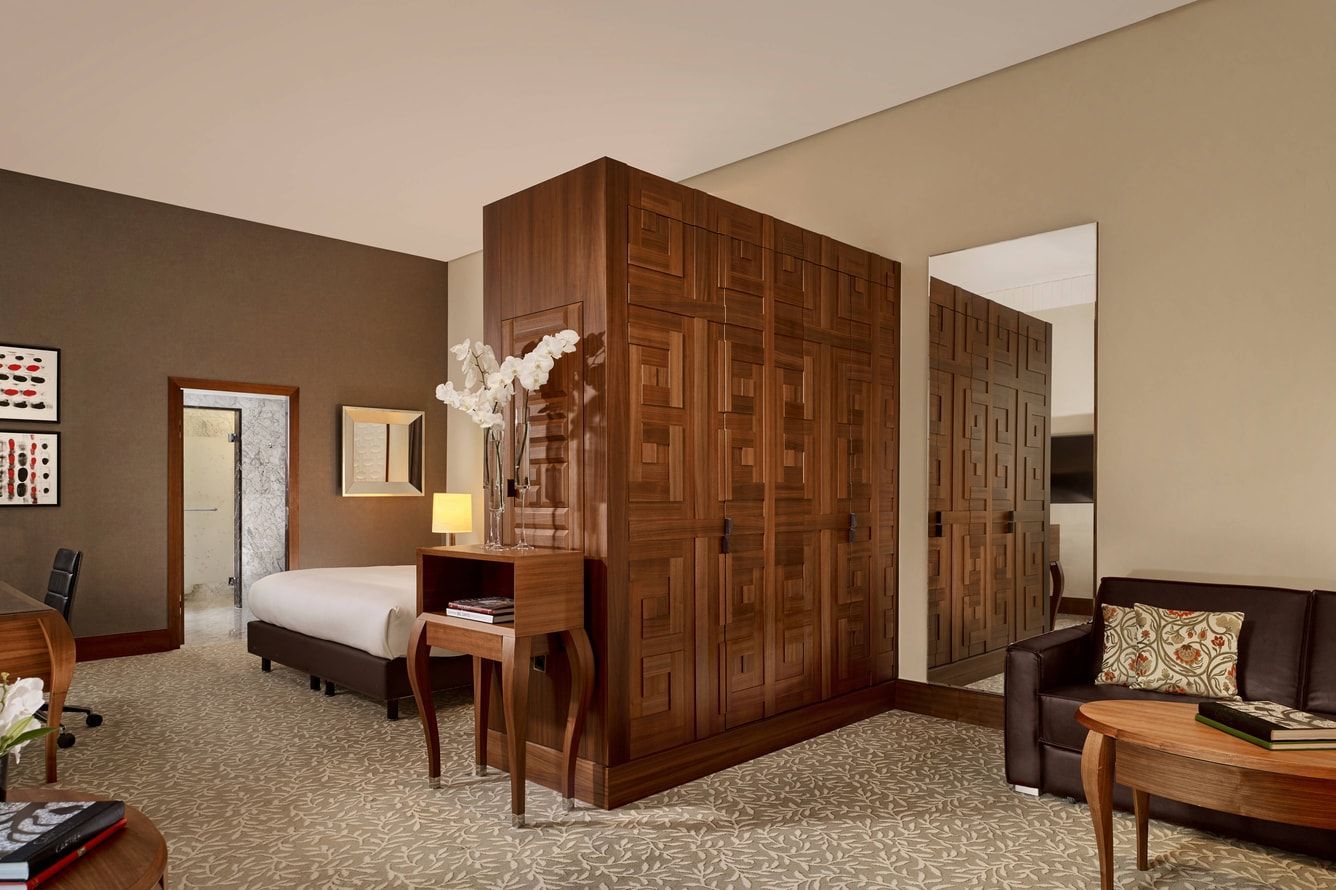 Hotel room with bed, wooden partition, desk, chair, and sitting area in neutral tones Ritz Carlton VIENNA 