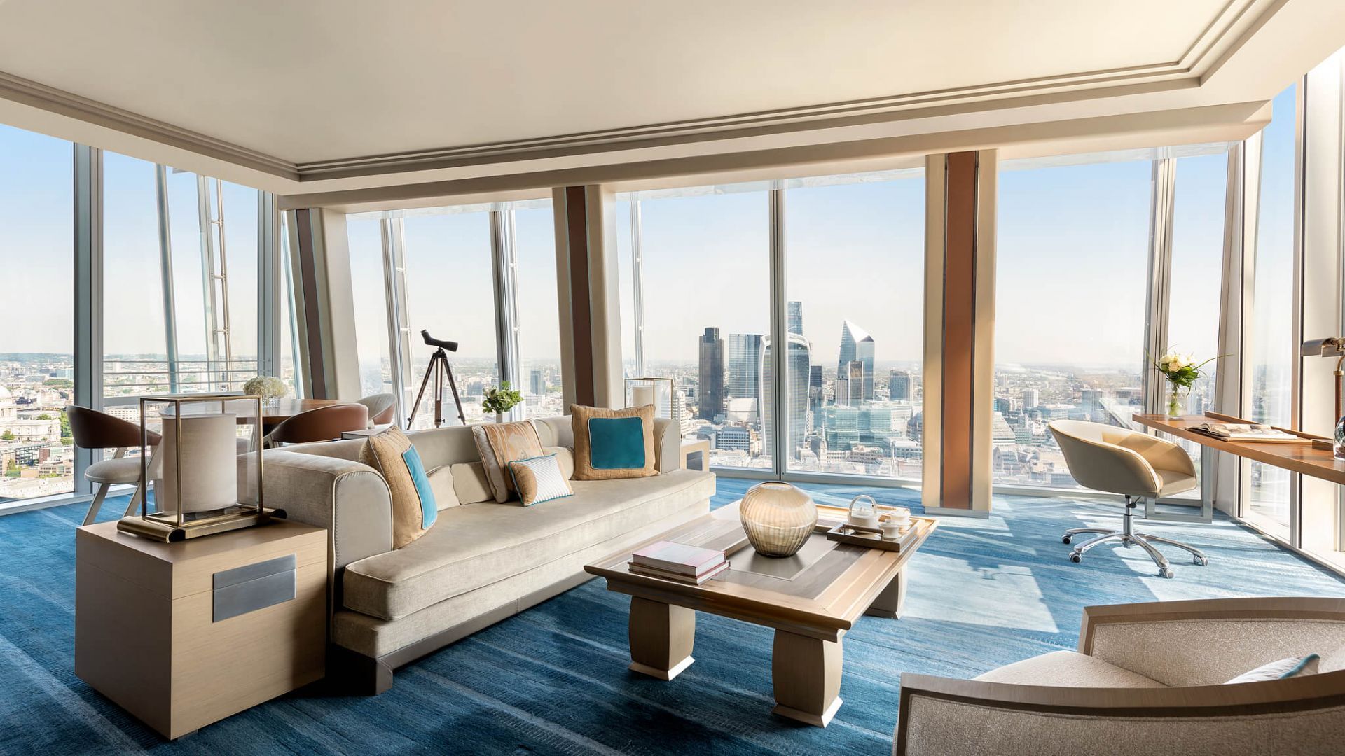 Luxury living room with city view, large windows, sofa, desk, and blue carpet. Shangri-La The Shard, London Bridge