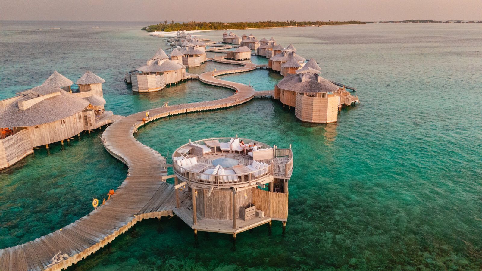 Overwater bungalows with thatched roofs and wooden walkways in turquoise water. 