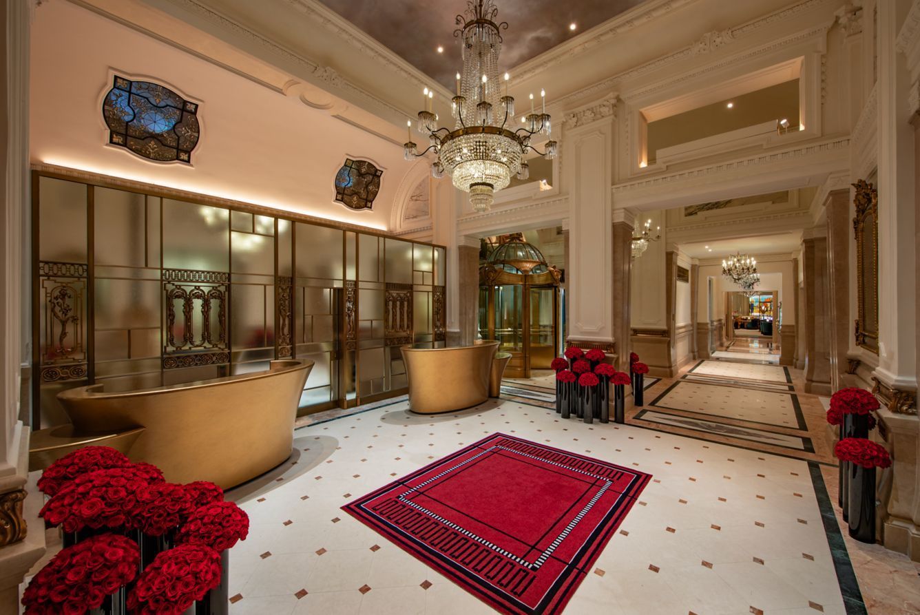 Elegant hotel lobby with gold accents, red rug and floral arrangements. St. Regis New York hotel