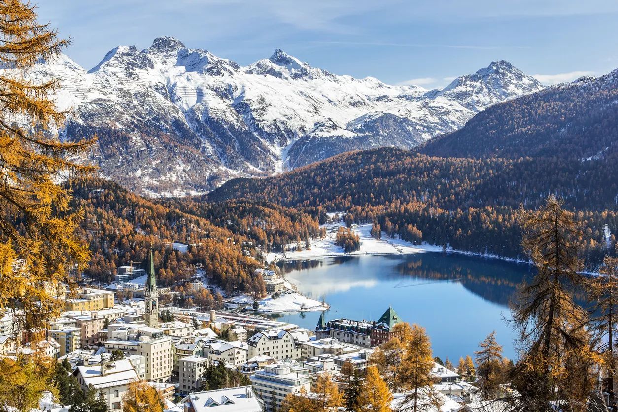 Snowy mountains overlooking a town by a lake in St. Moritz, Switzerland, in autumn.