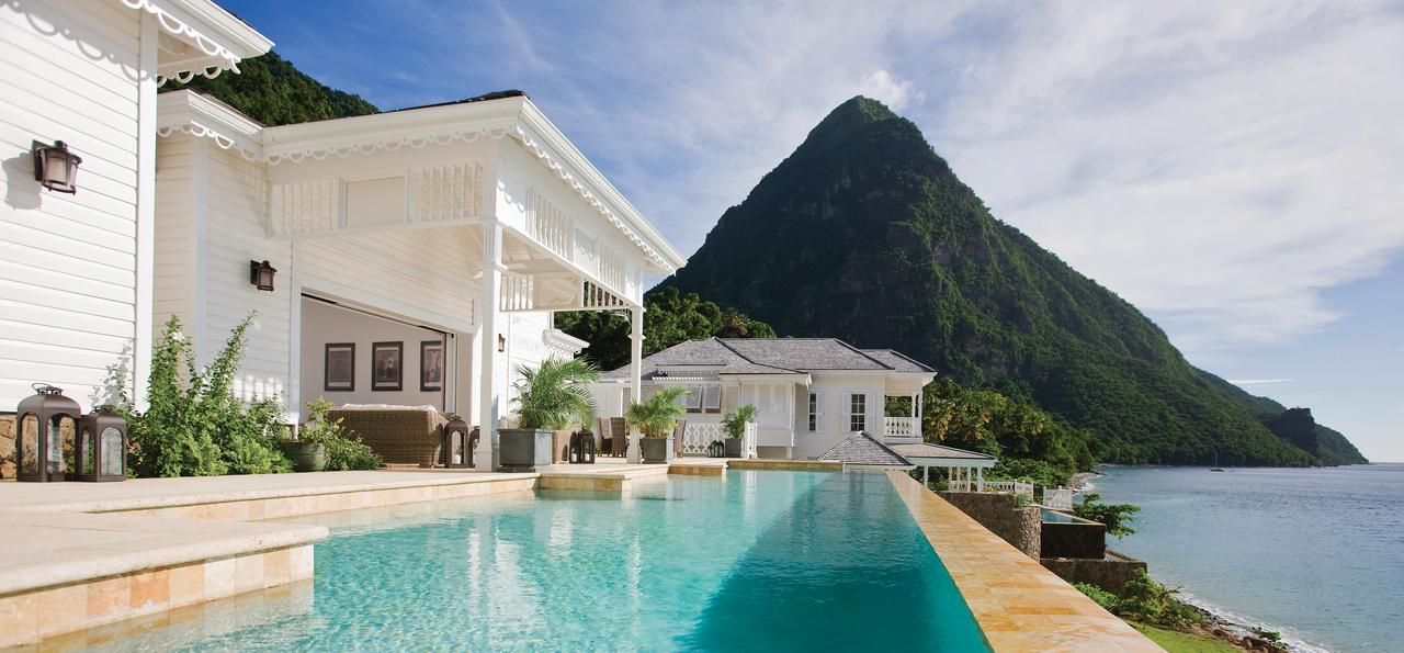 An infinity pool overlooking the Caribbean Sea with the lush green Piton mountains in the background under a blue sky. St Lucia