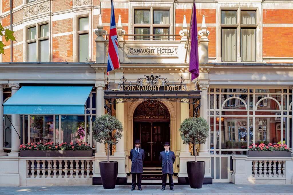 Exterior of the Connaught Hotel, London; two uniformed doormen stand at the entrance under a Union Jack flag.