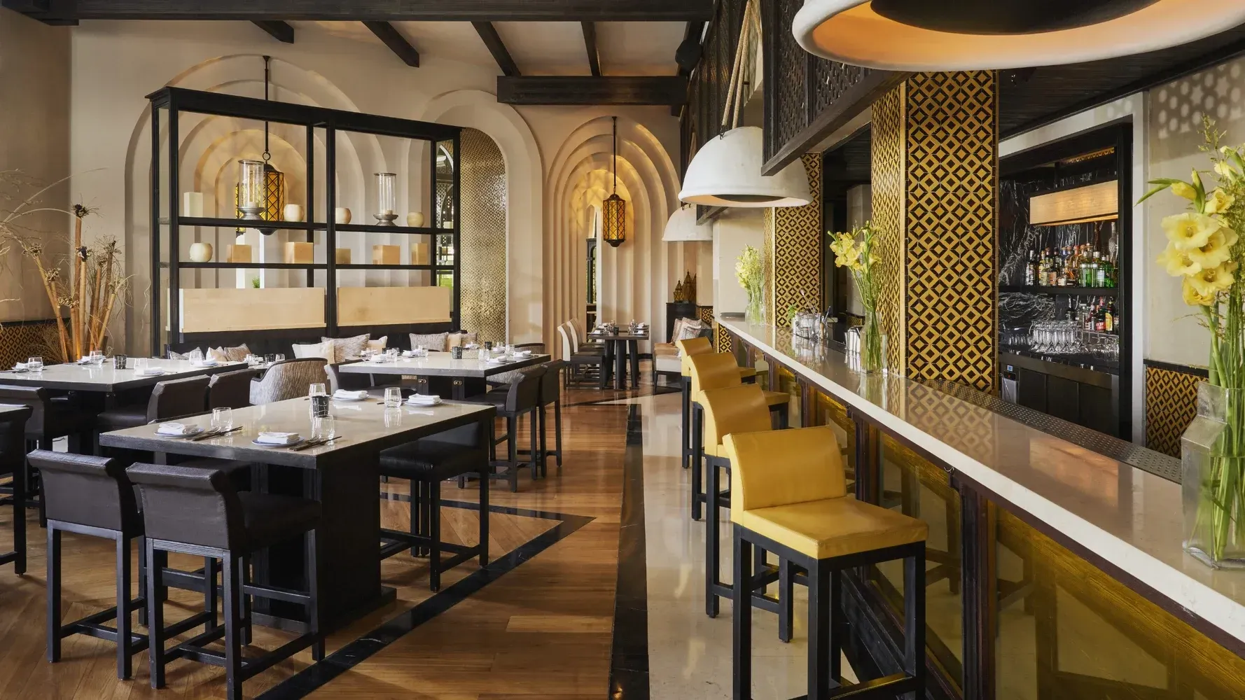 Upscale restaurant interior with bar seating, tables, and decorative archways; gold and neutral tones.