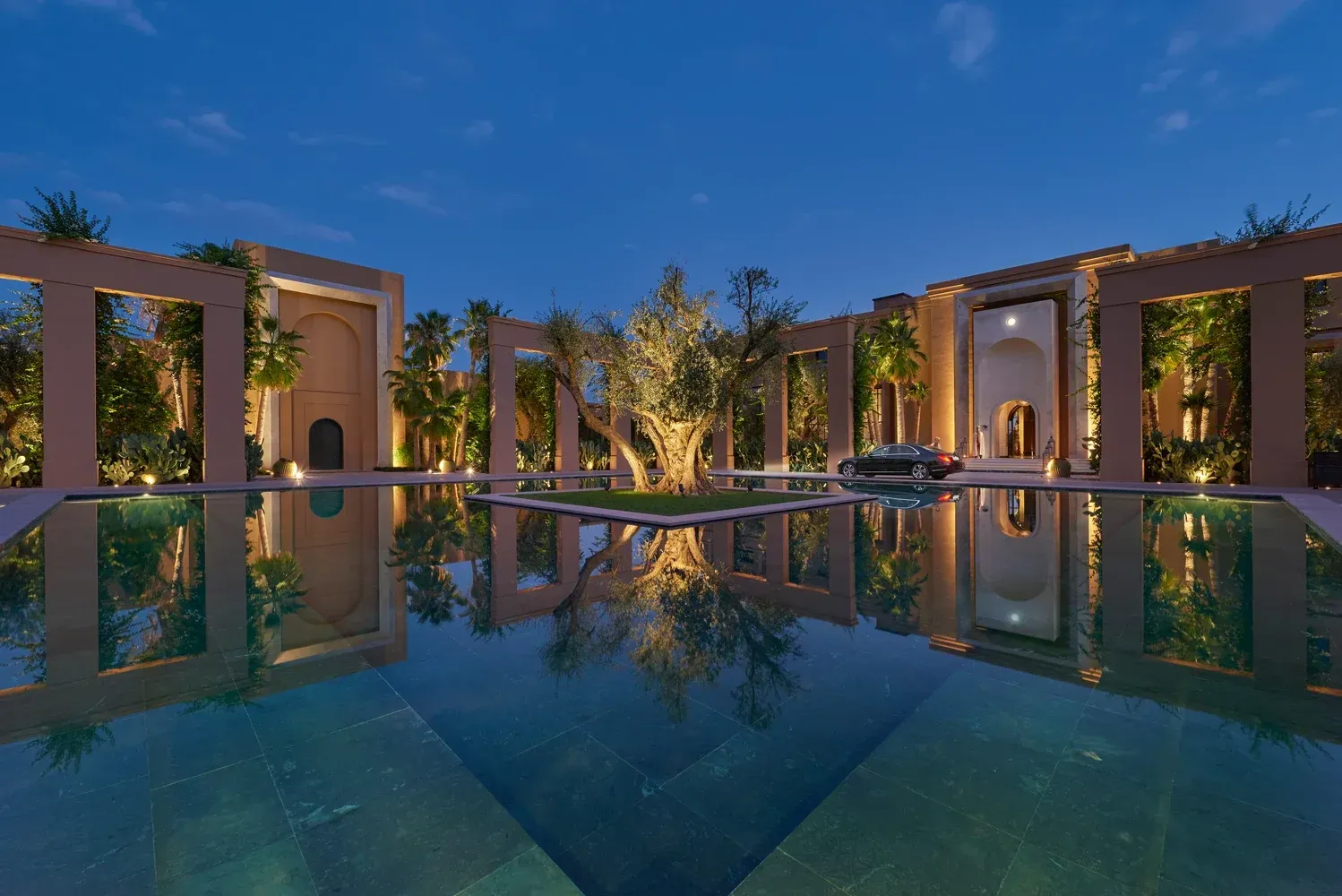 Reflective pool in courtyard at dusk, mirroring lit architecture and trees.