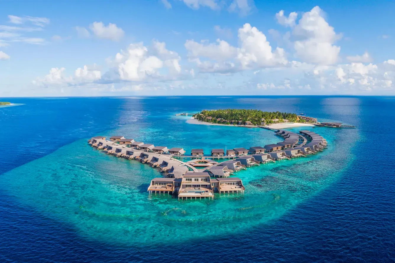 Aerial view of a tropical island with overwater bungalows and clear turquoise water. Maldives