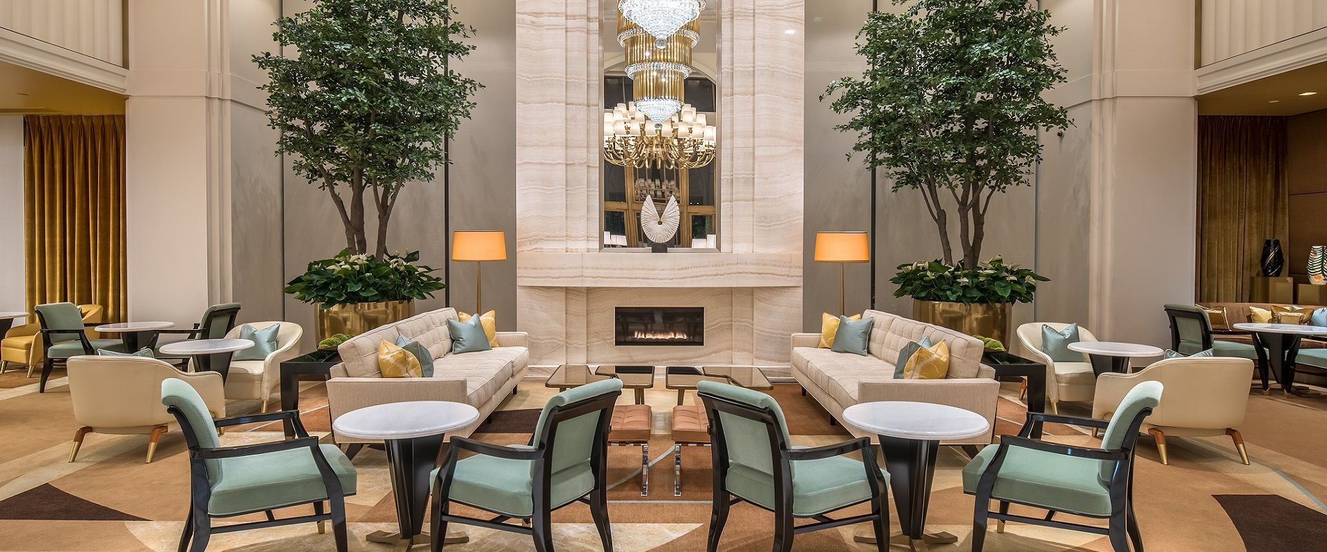 Elegant hotel lobby with couches, chairs, trees, and fireplace, under a grand chandelier. Lobby The Waldorf Astoria, Beverly Hills: