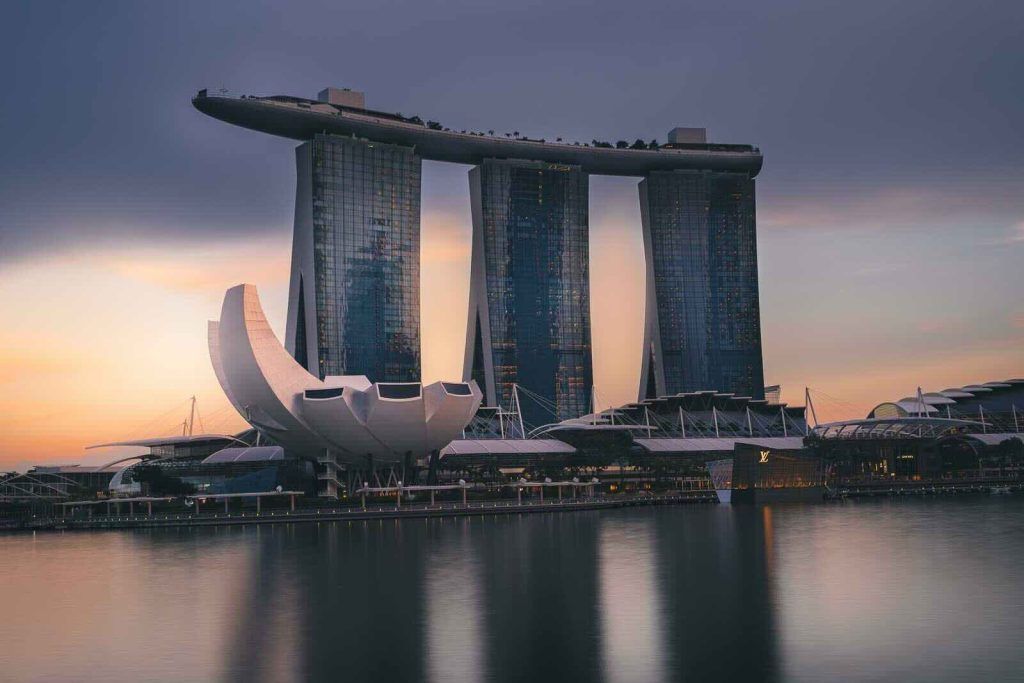 Marina Bay Sands and the ArtScience Museum in Singapore at twilight, with the city buildings reflected in the calm water.