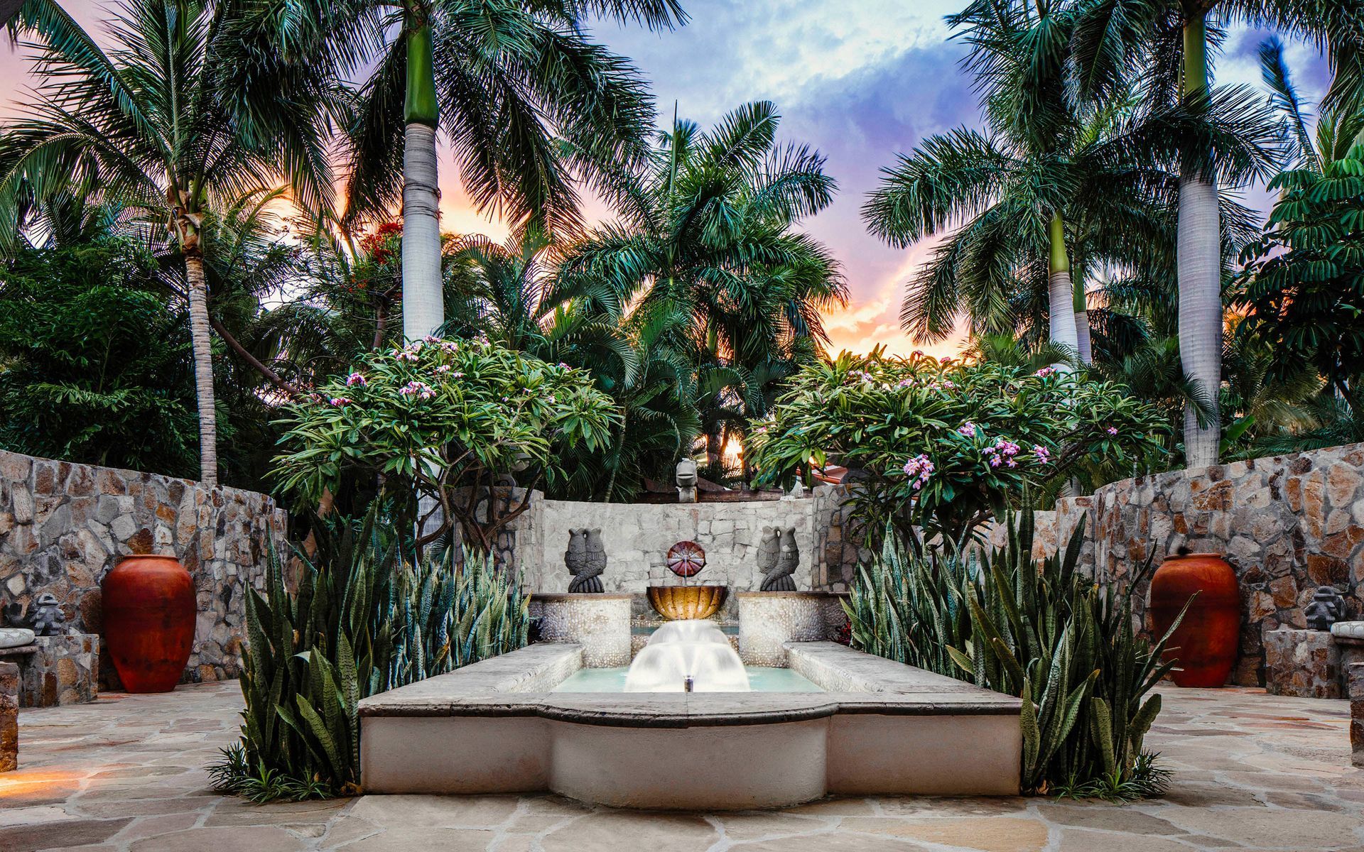 Tropical courtyard fountain at sunset, surrounded by palm trees and lush greenery
