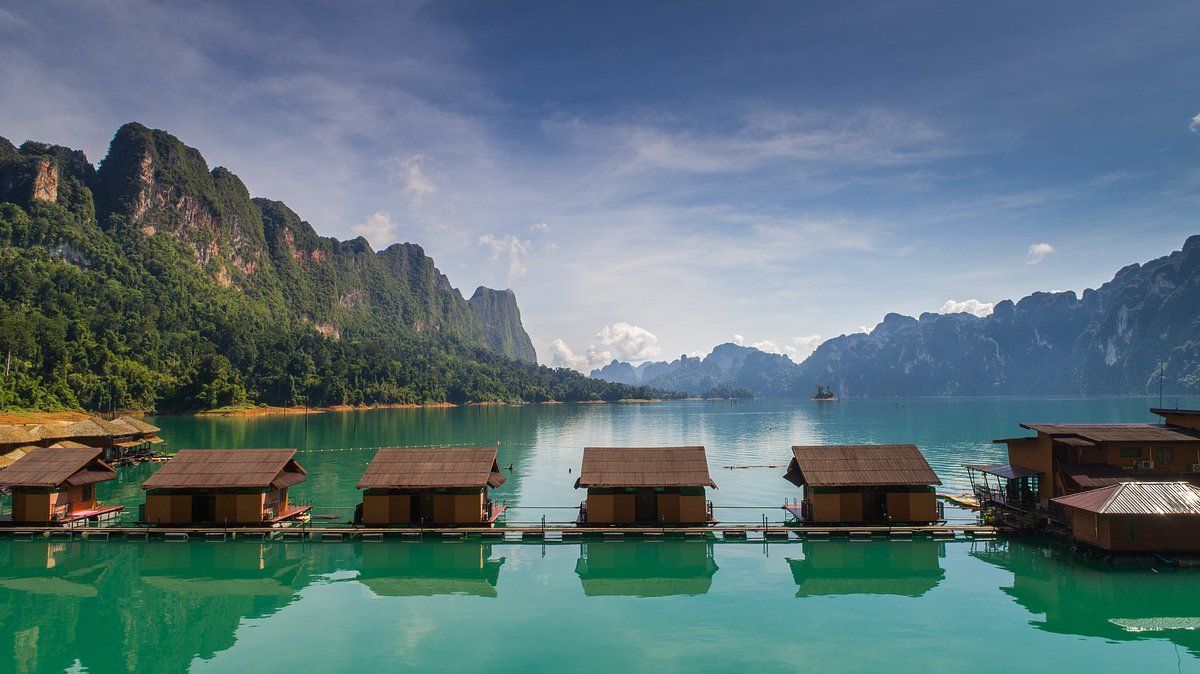 Floating cabins on turquoise water, set against lush mountains under a blue sky.