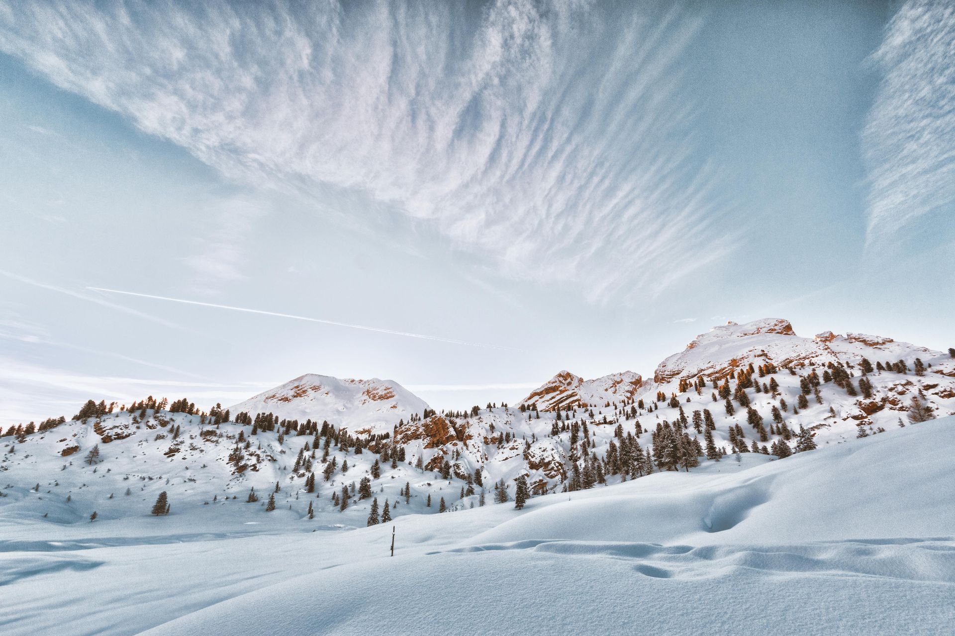 Snowy mountain landscape under a bright, cloud-filled sky. Snow covers mountains and foreground.  Luxury Ski Holidays in the Dolomites
