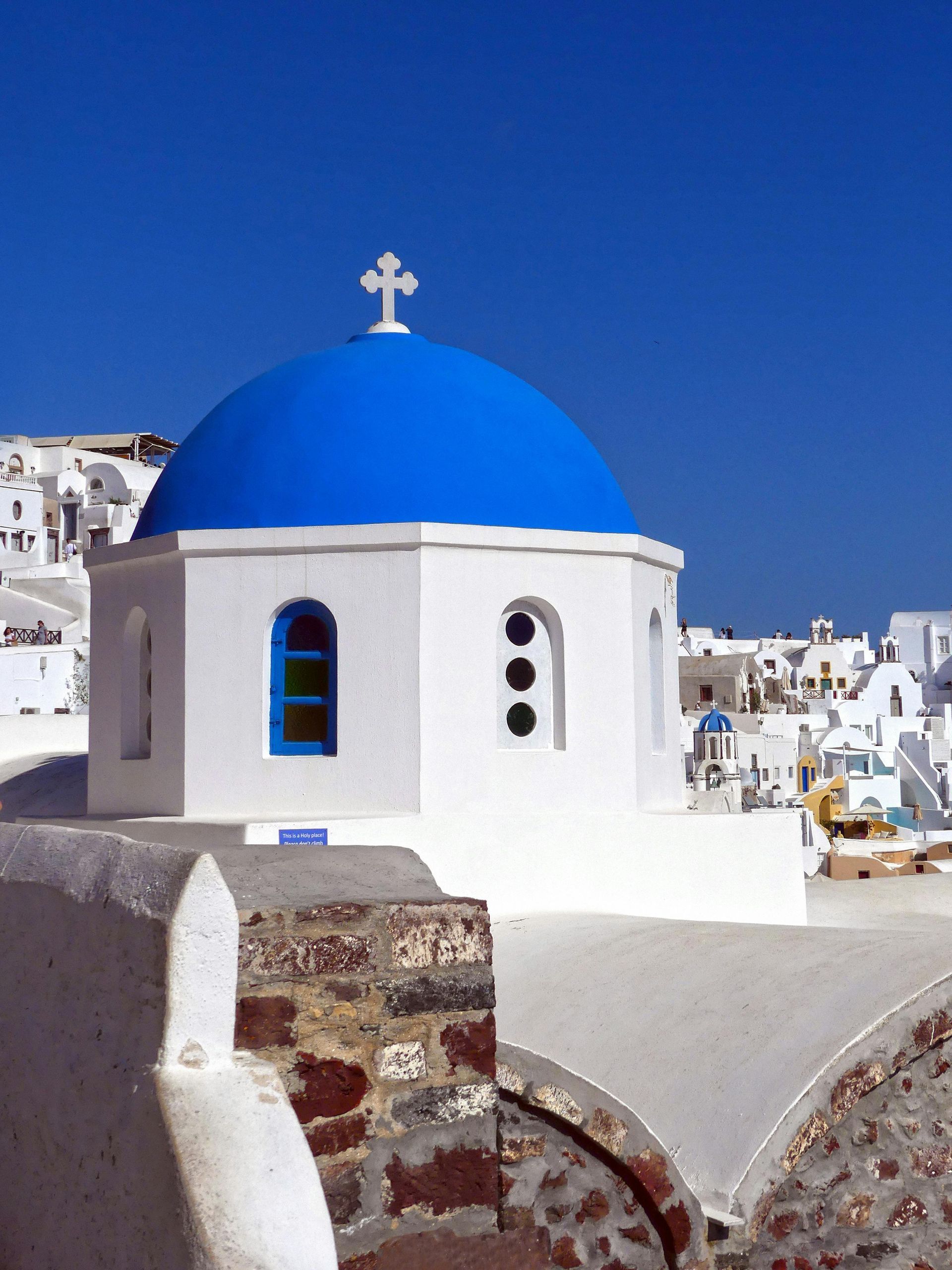 White and blue domed church in Santorini, Greece, under a bright blue sky. Akrotiri