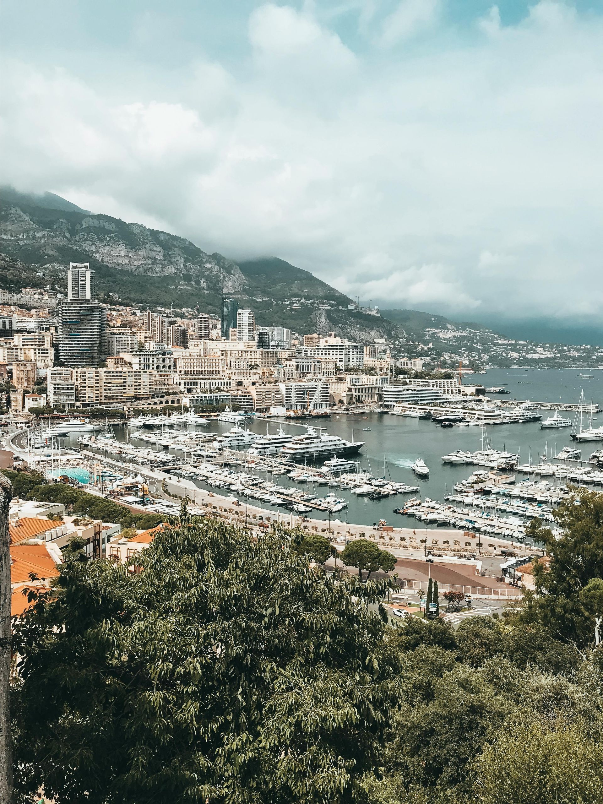 Coastal city with harbor full of boats, buildings on hills under cloudy skies.French Riviera