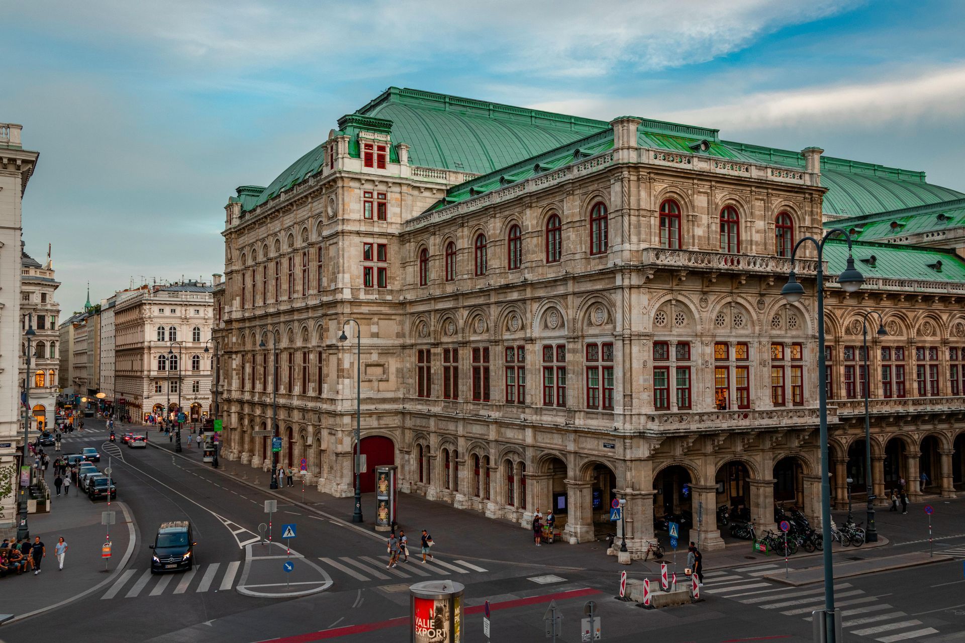 Grand historic building with a green roof on a city street with cars and pedestrians Vienna