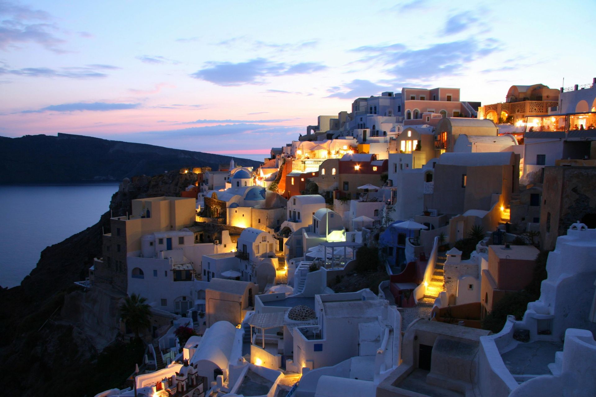 Whitewashed buildings on a cliffside, lit at dusk; Santorini, Greece.