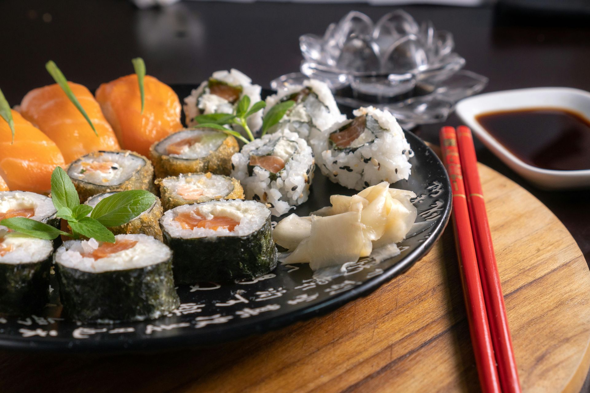 Sushi platter with rolls, nigiri, and ginger, red chopsticks, and soy sauce.