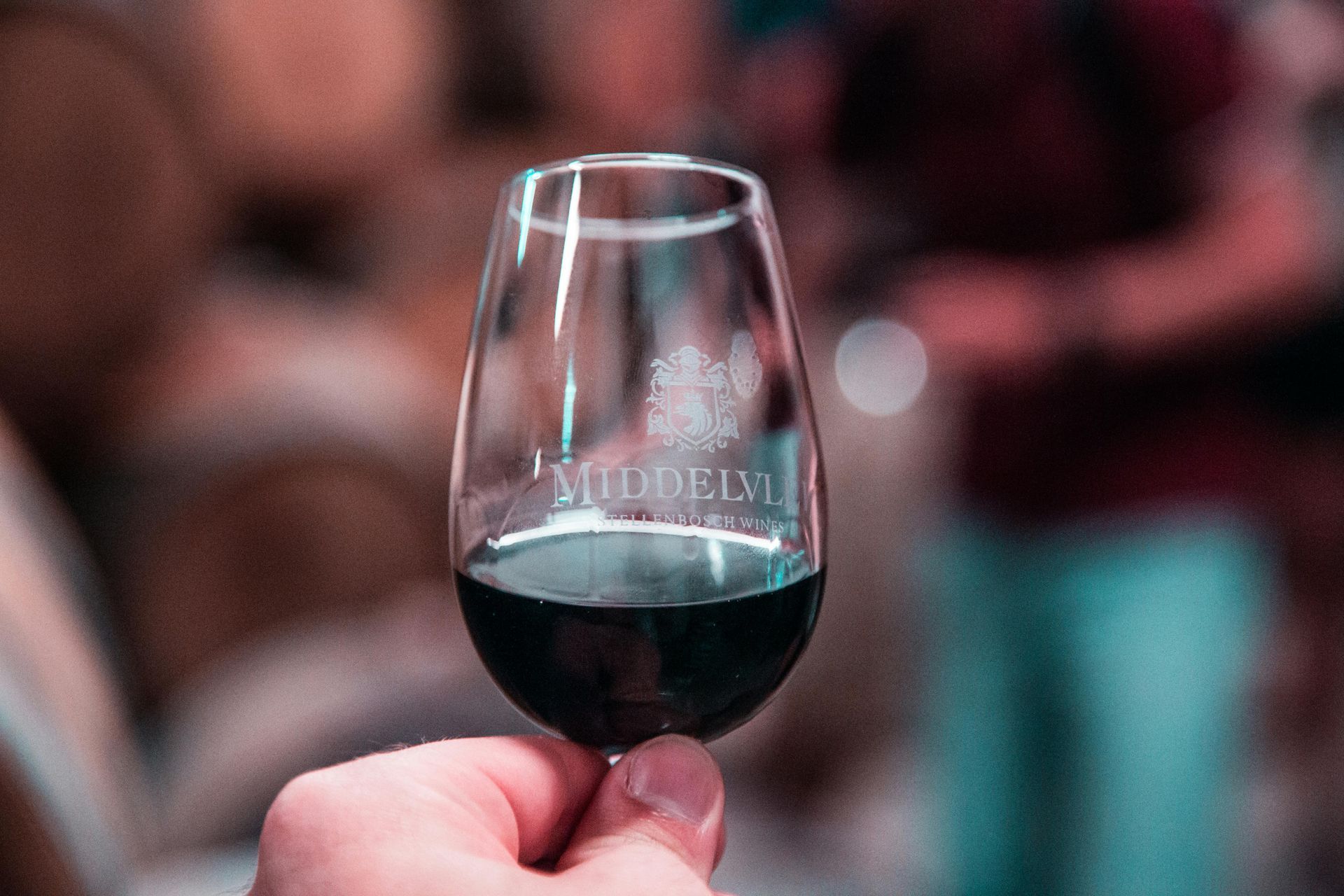 A hand holds a glass of red wine, etched with the word