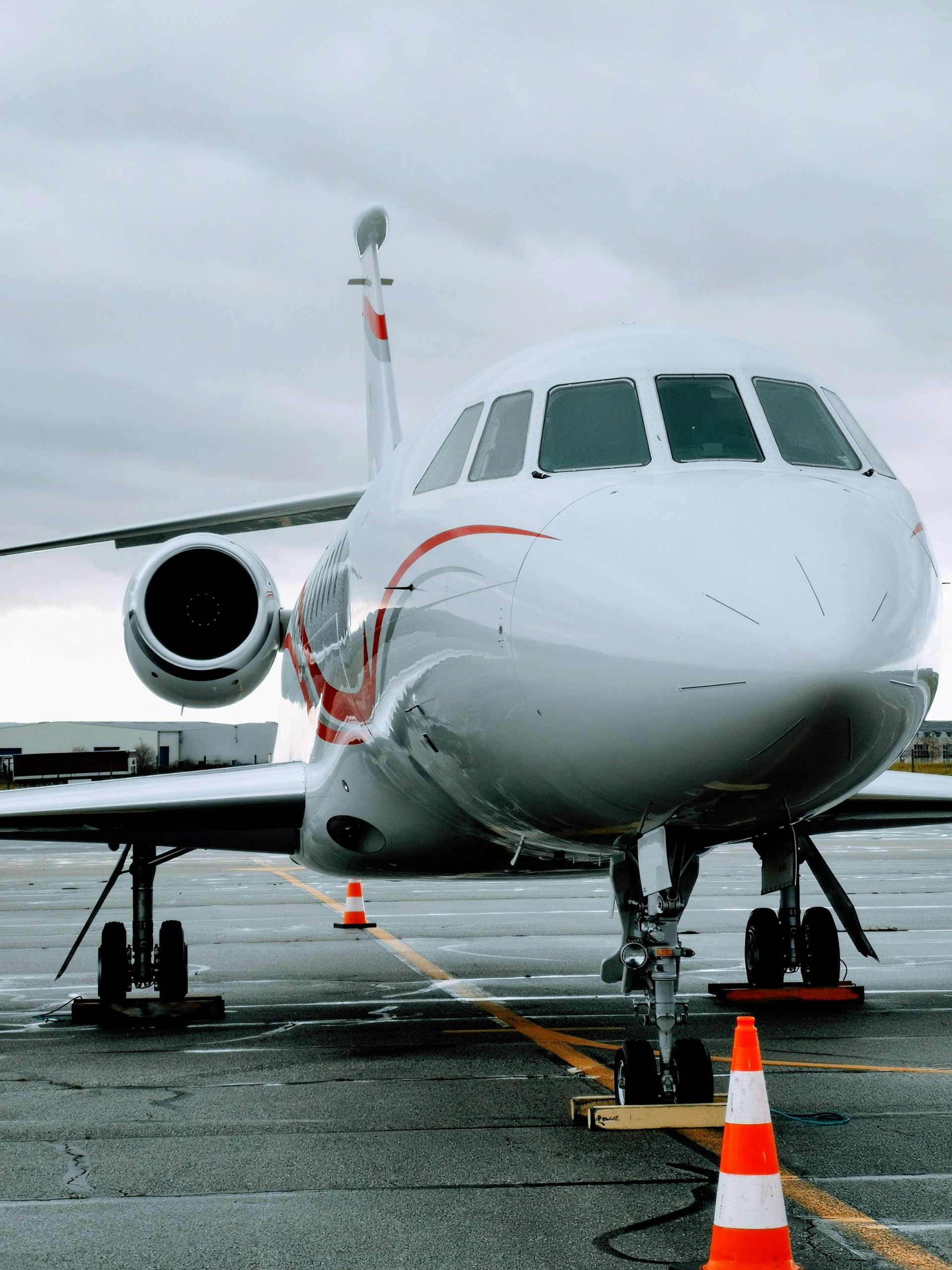 White private jet on a tarmac, red accents, under cloudy sky, orange safety cones.