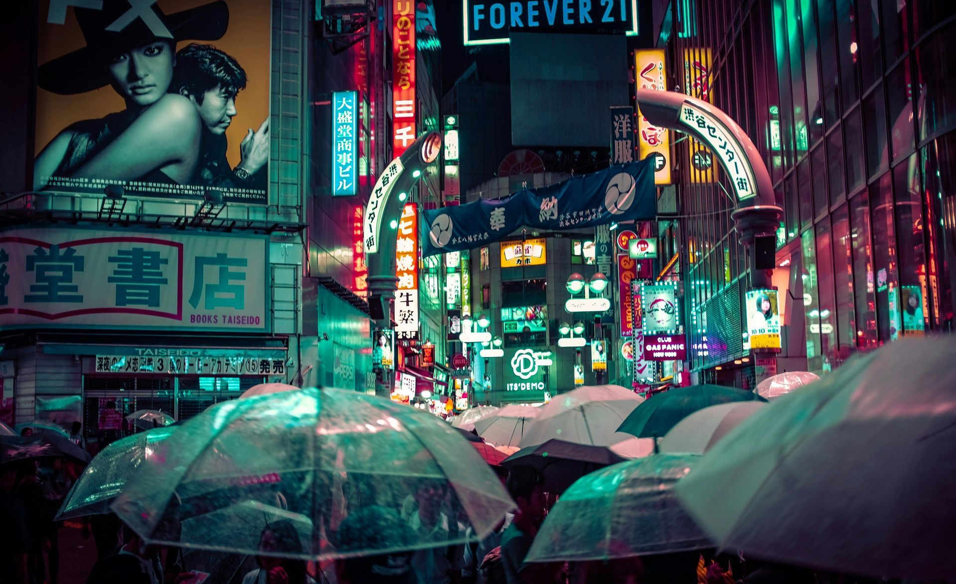 Rain-slicked Tokyo street at night, neon lights ablaze, umbrellas, crowds of people.