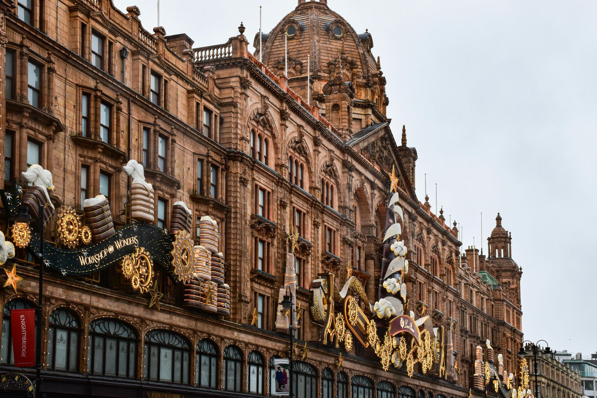 Exterior view of Harrods department store, London. Brown brick facade with ornate gold decorations and a domed roof.