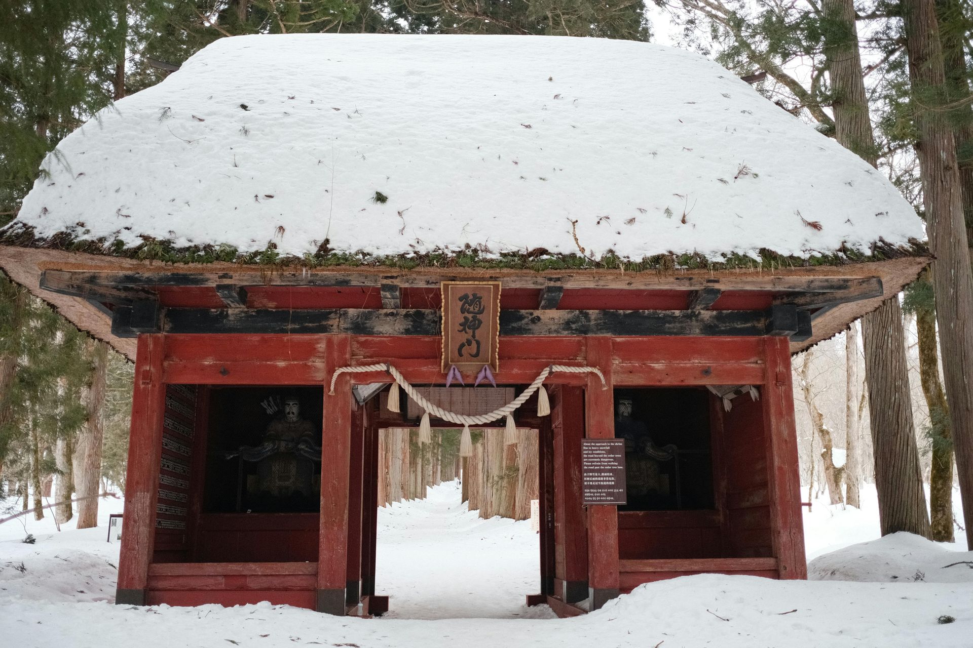 Red torii gate covered with snow in a snowy forest; the gate has a thatched roof, and is an entrance to a Japanese shrine. Niseko, Japan