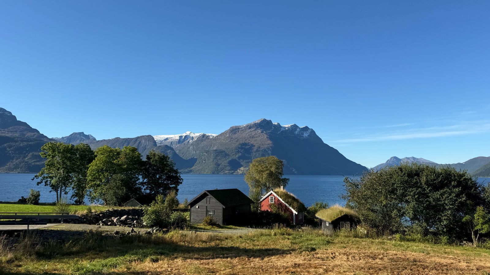 Traditional turf-roofed cabins beside a Norwegian fjord and mountains