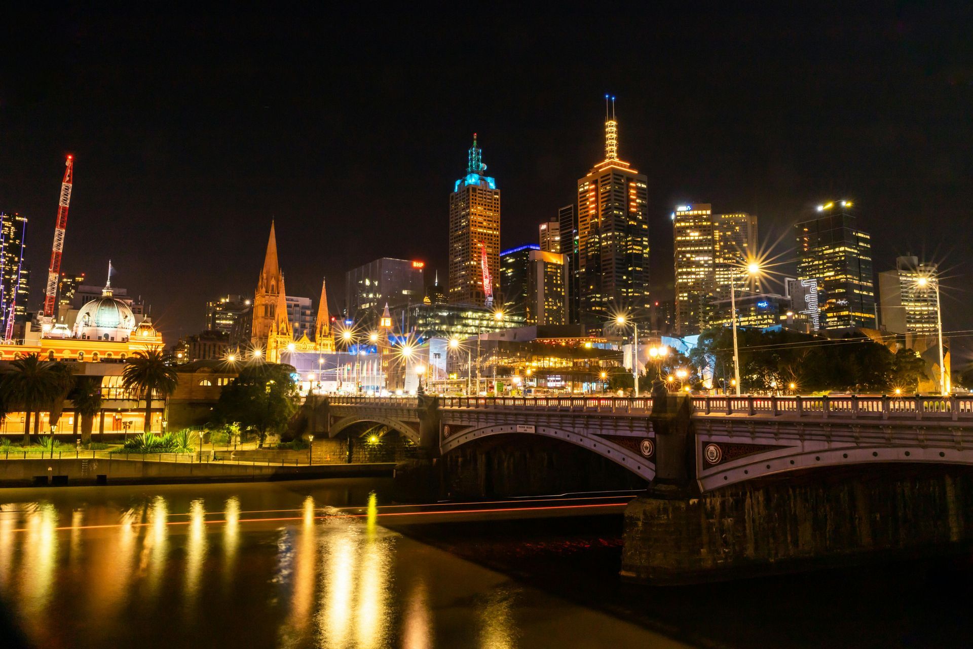 Night view of Melbourne, Australia, skyline with illuminated skyscrapers reflected in the Yarra River, and a bridge.