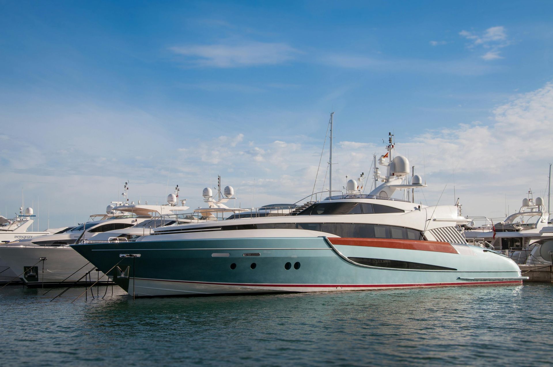 A large teal and white yacht docked in a harbor with a blue sky.