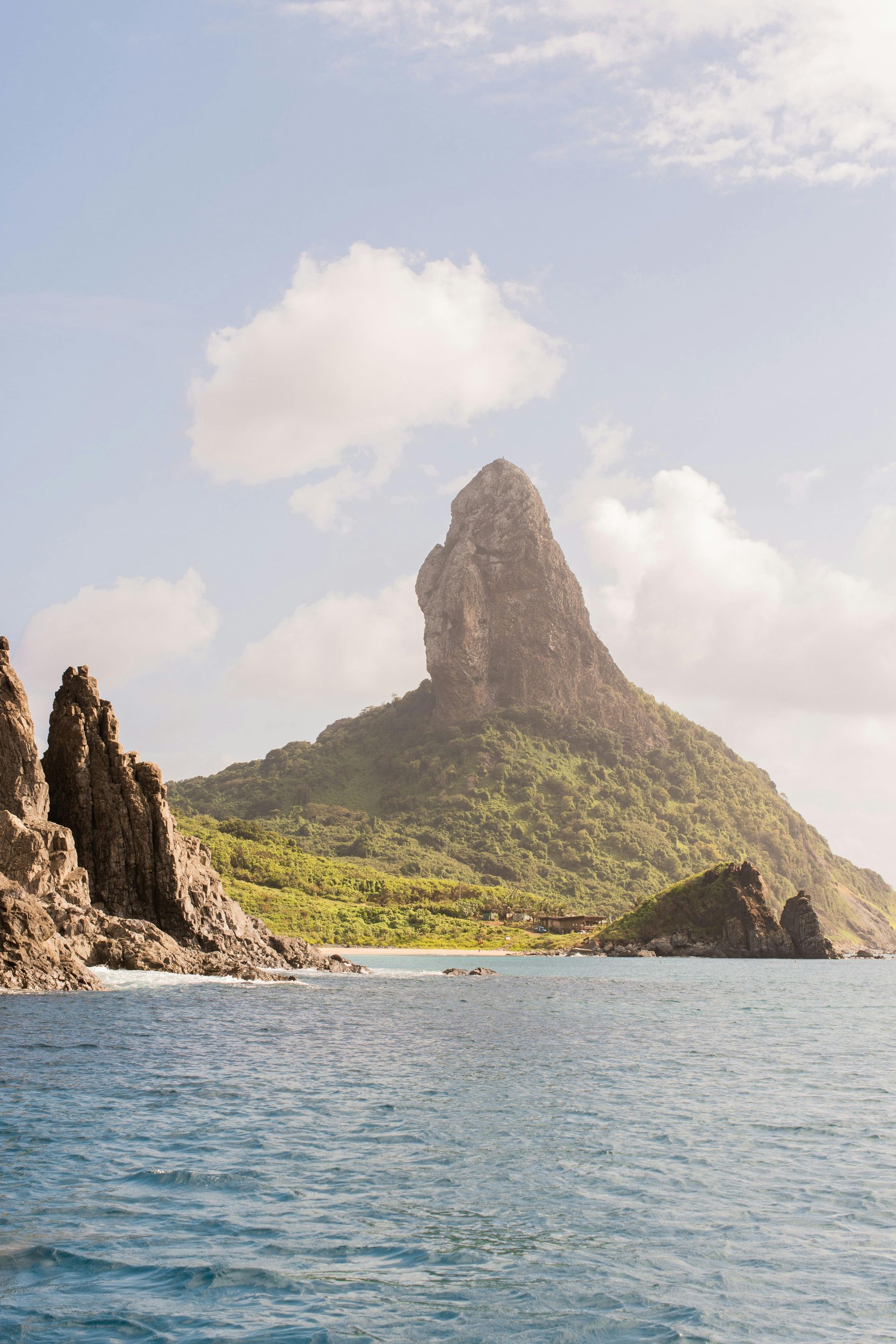 Rocky island with a tall green peak rising from the sea under a cloudy sky