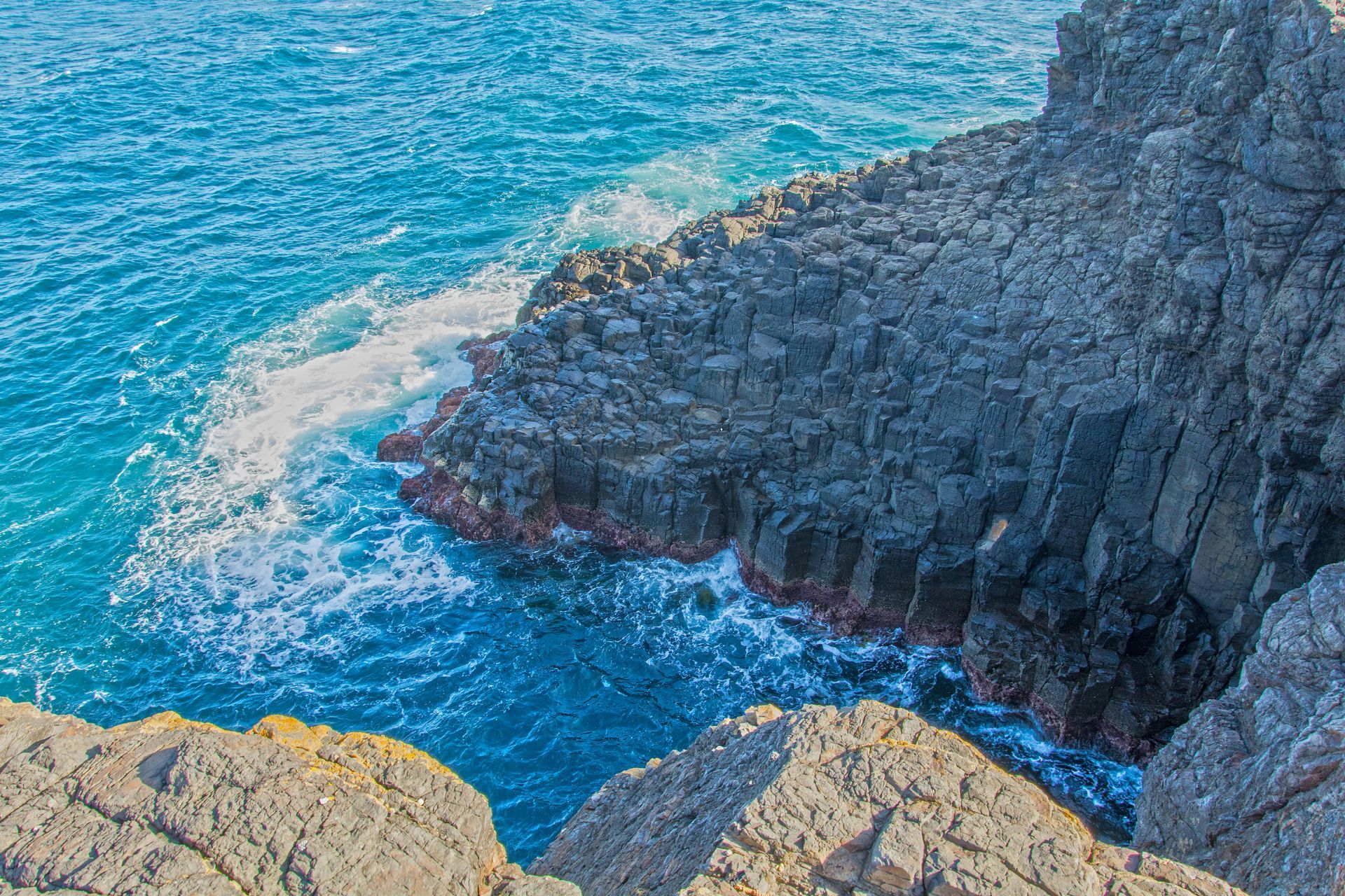 Ocean waves crashing against dark, rocky cliffs; blue water.