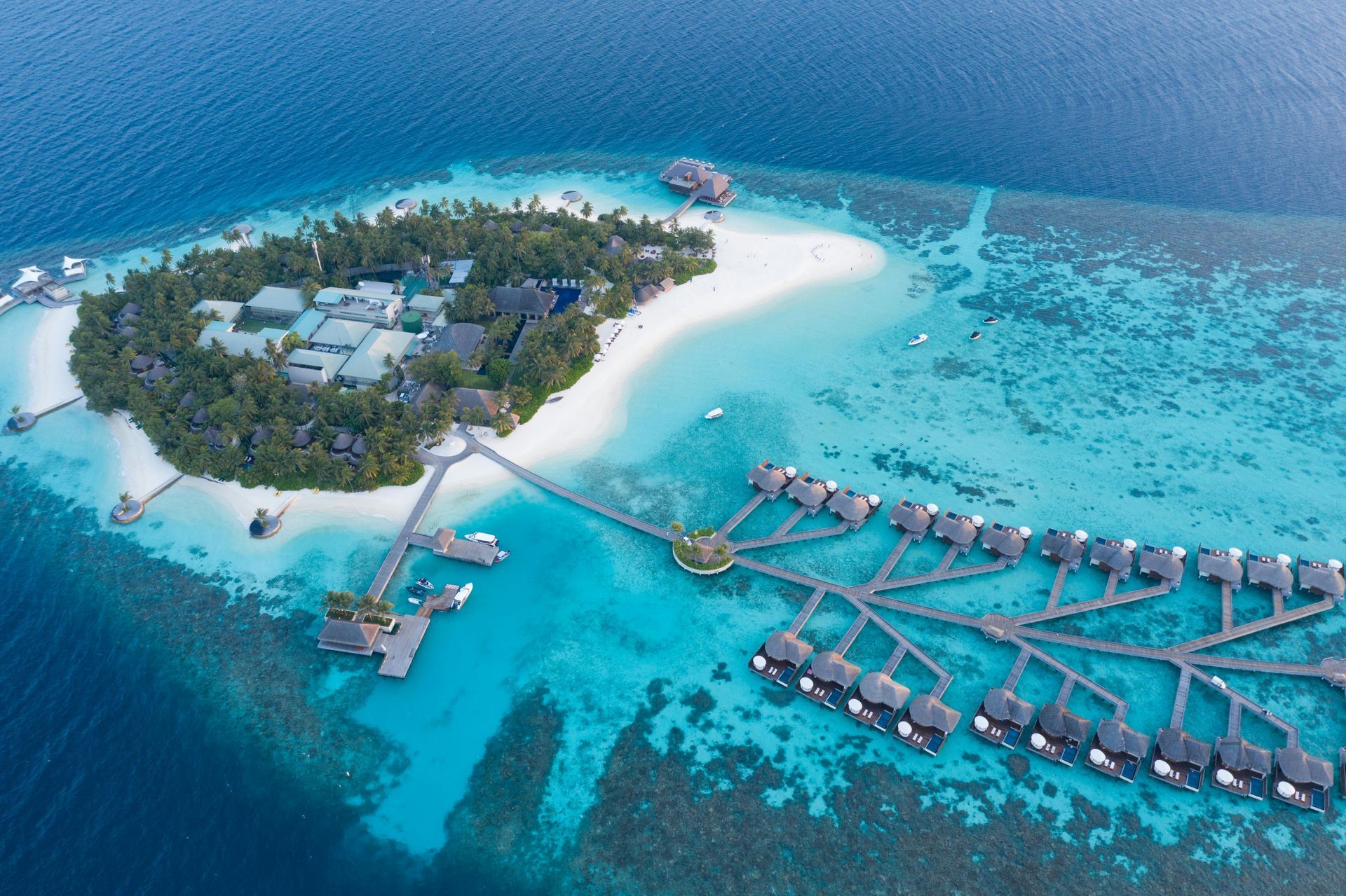 Aerial view of a tropical island resort. Turquoise water surrounds the lush green island with overwater bungalows. Fiji