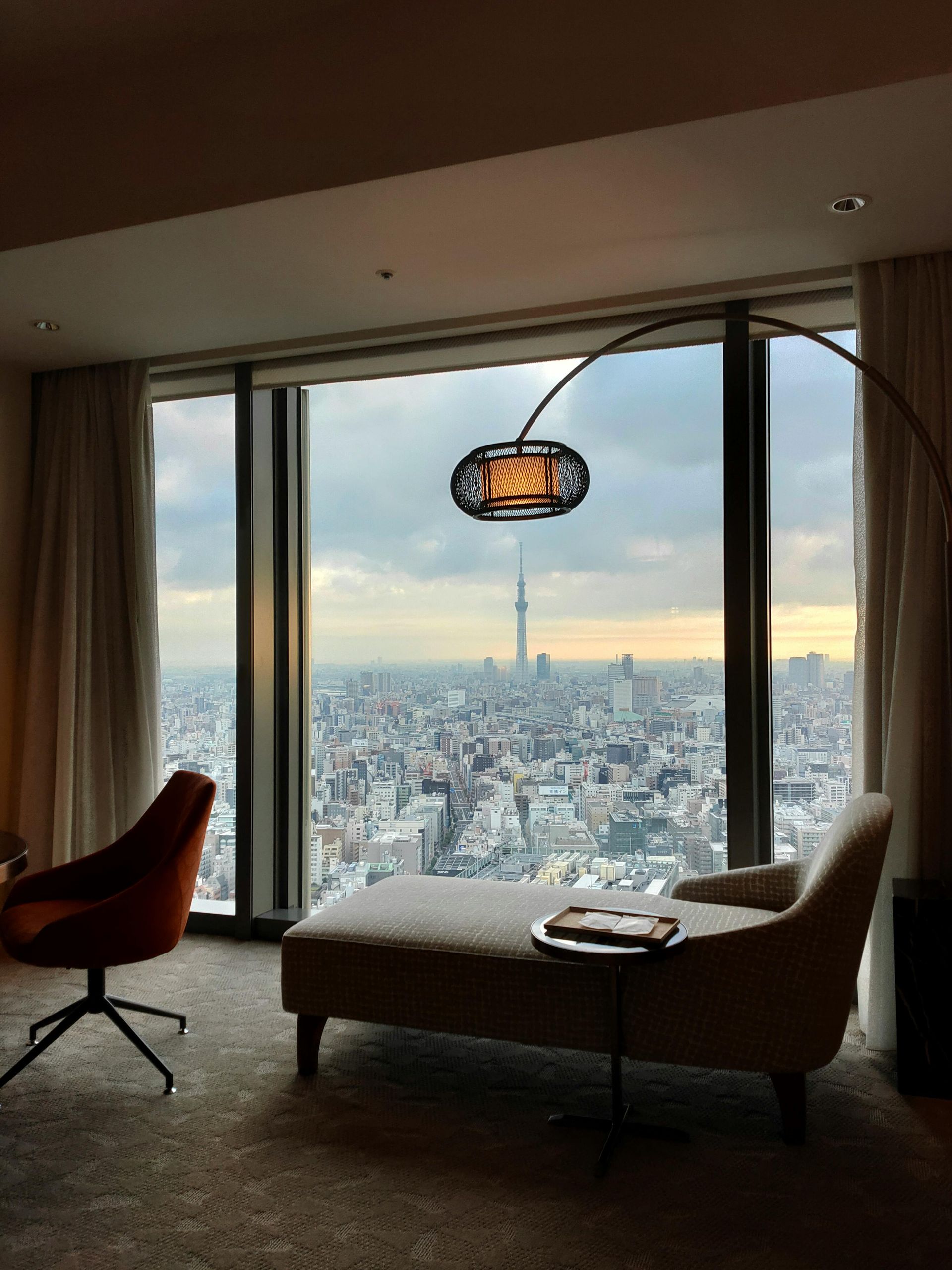 Interior of a dimly lit bar with illuminated wooden surfaces and shelves, and a bartender serving drinks. Tokyo hotel Mandarin Oriental, Tokyo