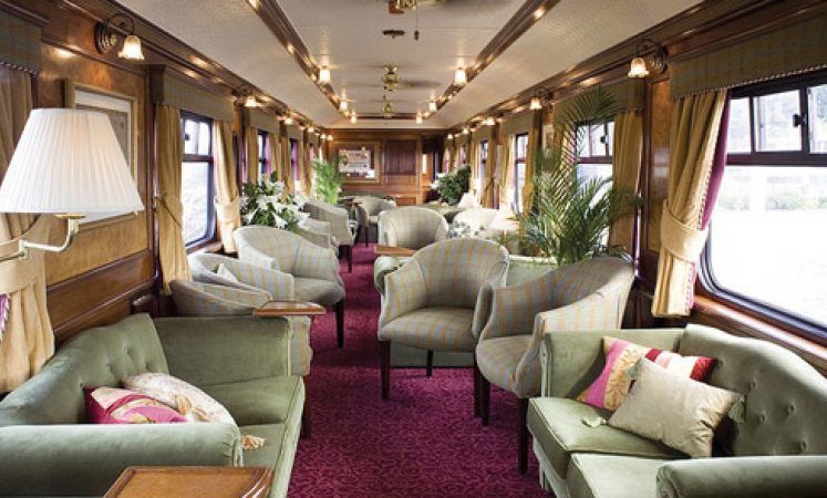Luxurious train car interior with green seating, wood paneling, and a red carpet. Belmond Royal Scotsman