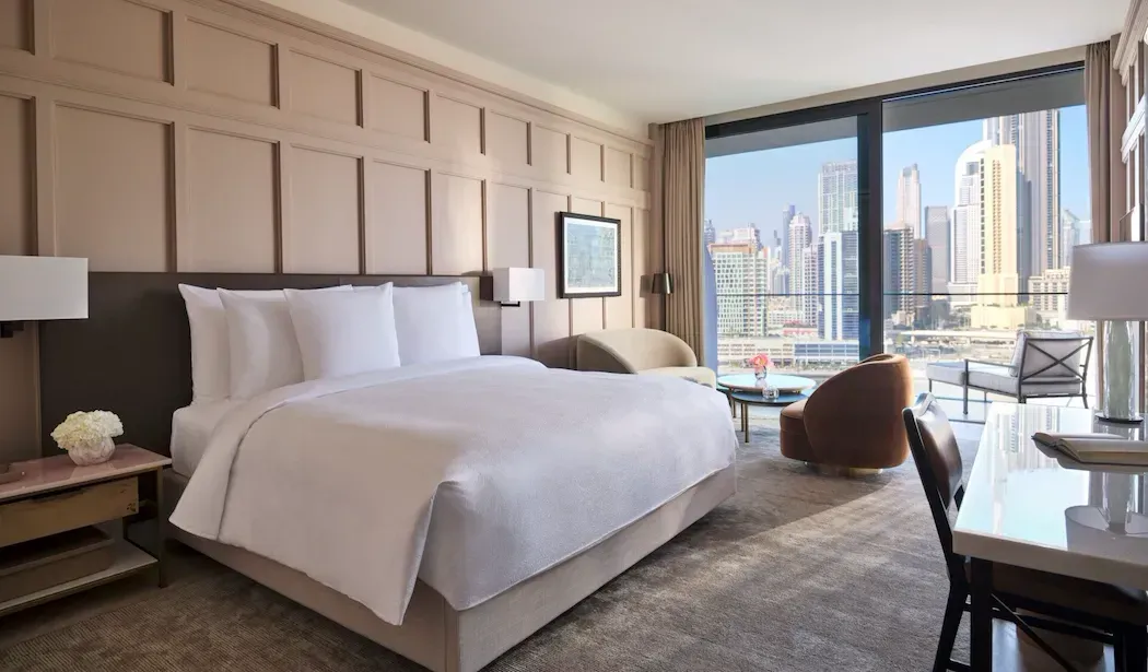 Hotel room with a large bed, city view window, desk, and seating area. Beige and neutral tones. The Lana, Dorchester