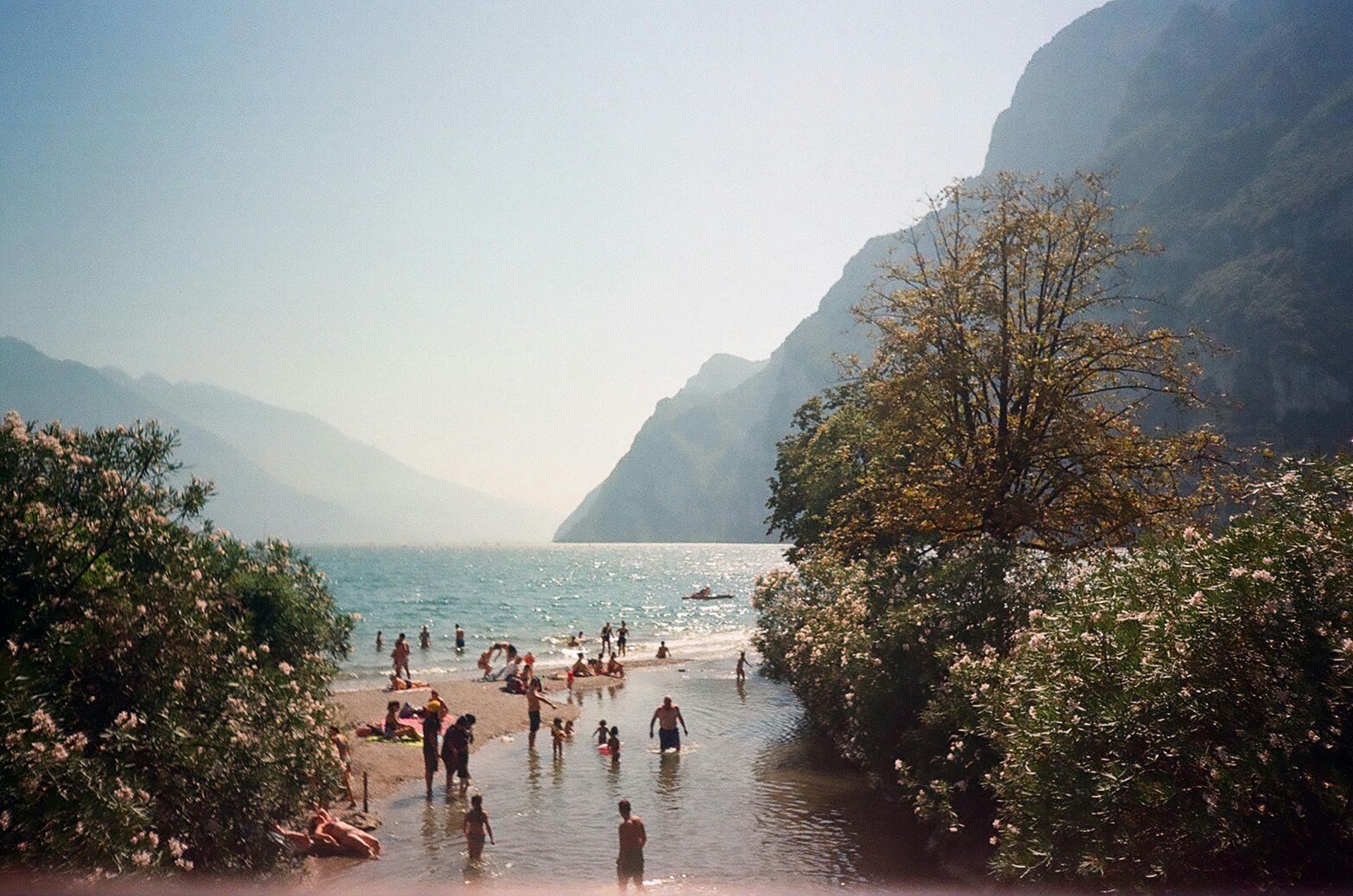 People swimming and relaxing on a beach with a mountain backdrop; a river flows into the sea.