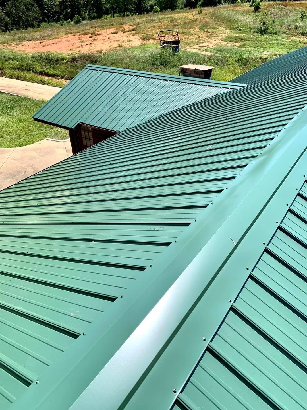 An aerial view of a green metal roof on a building, looking down the ridge line toward a grassy yard.