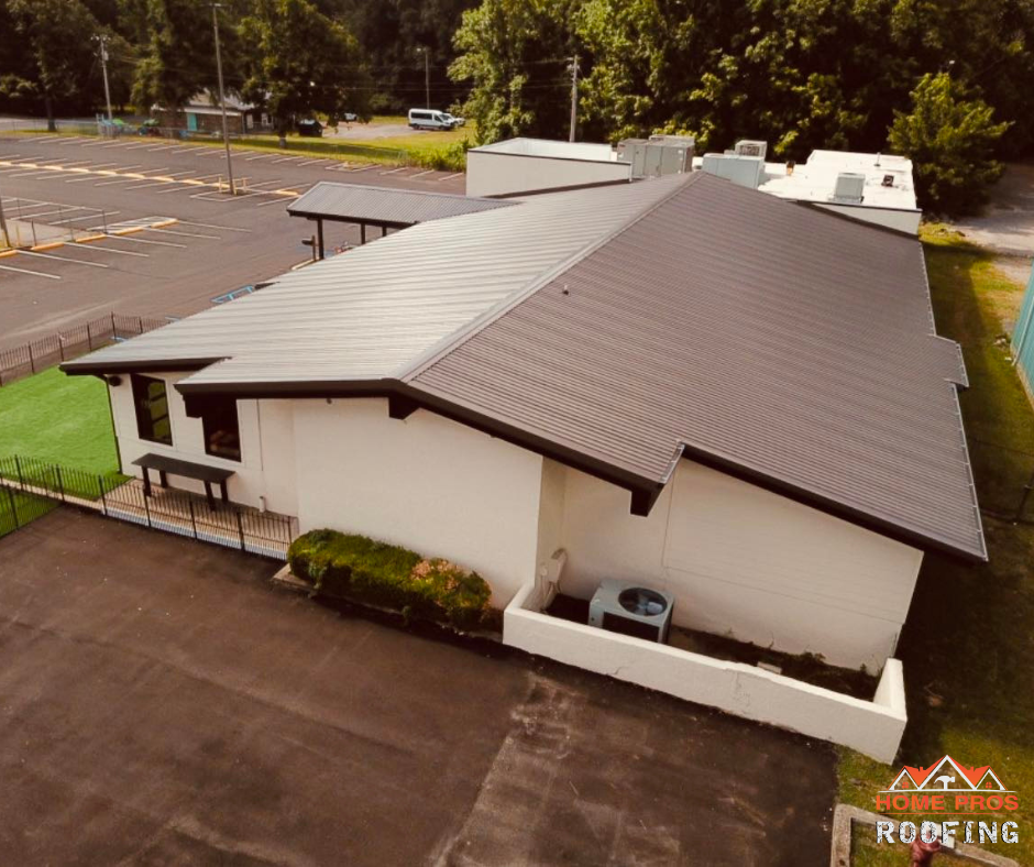 An aerial view of a building with a dark metal roof, beige exterior walls, and a parking lot.