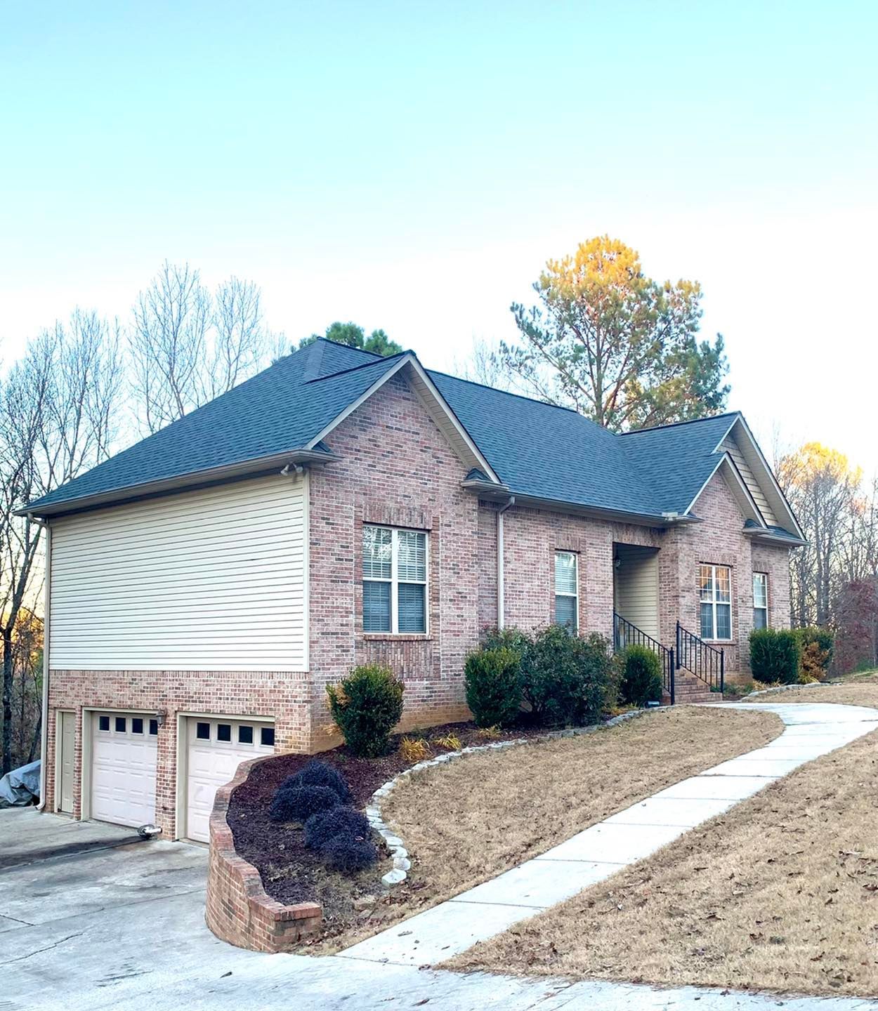 A single-story brick house with a two-car garage, light siding, and a concrete path leading to the front entrance.